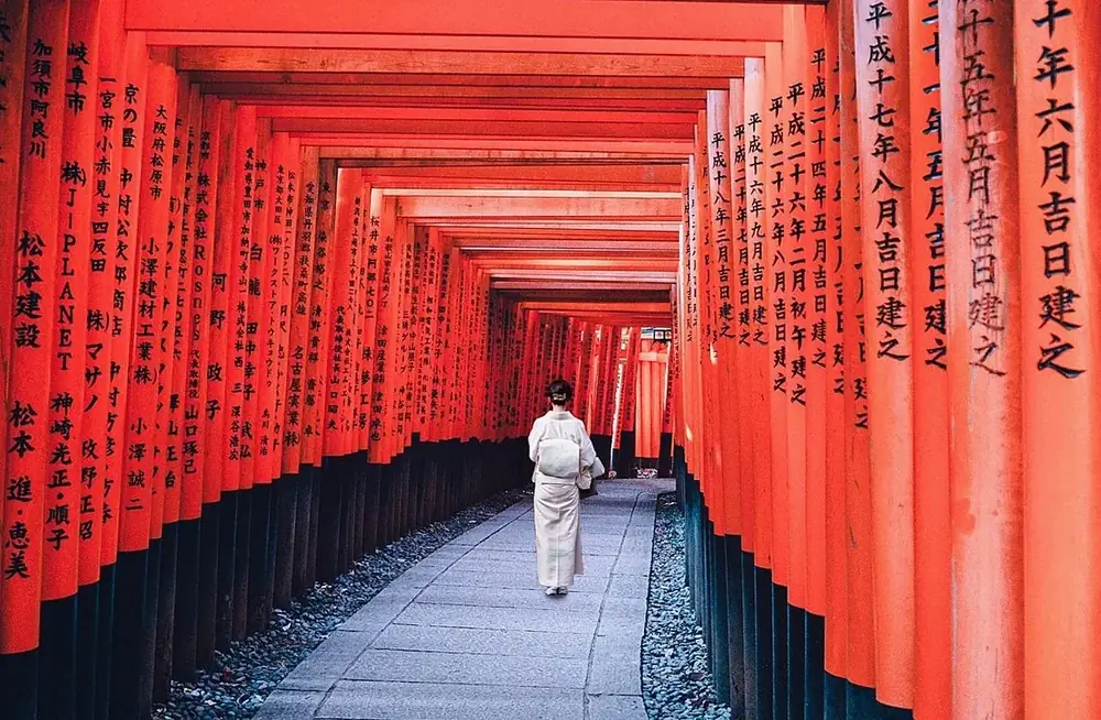 Visitor walking through a long corridor of red torii gates at a shrine in Japan