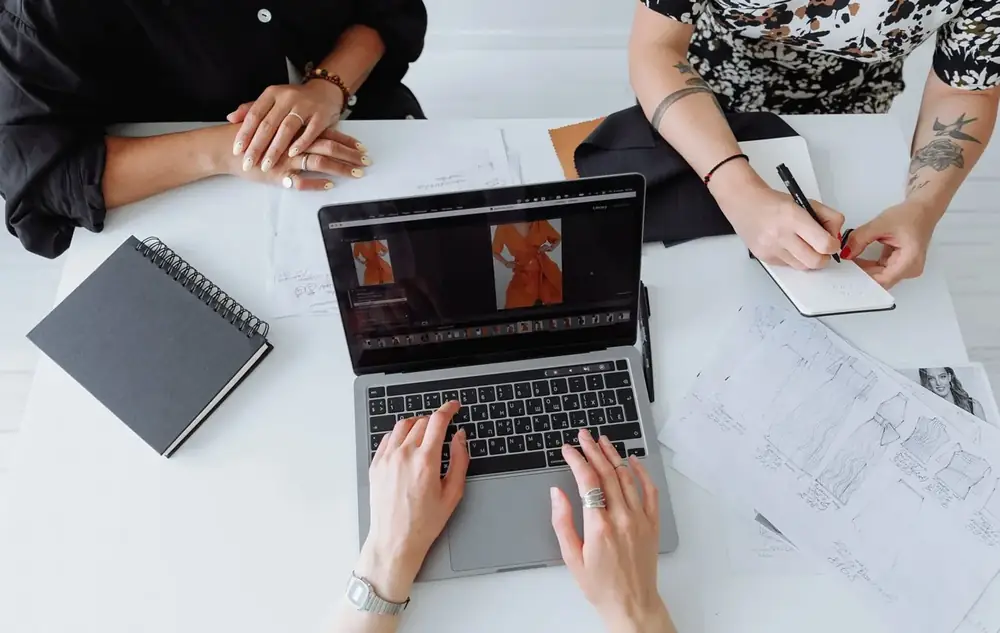 Overhead view of hands working at a laptop and notebook on a white table