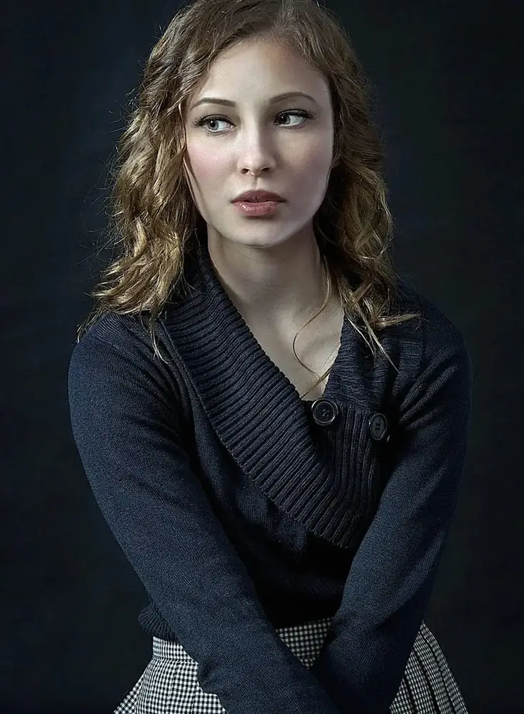 Woman with wavy hair in a navy knit cardigan and checked skirt